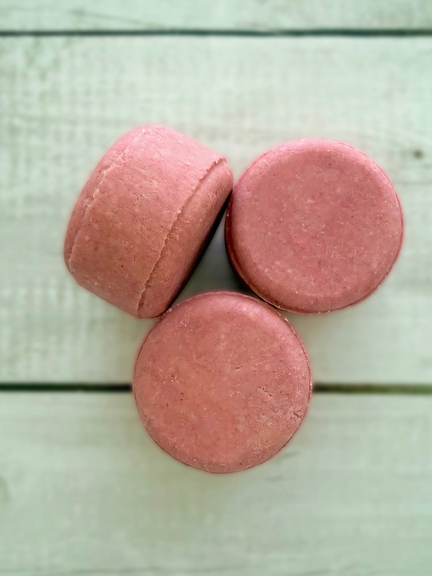 Three pink solid shampoo bars, arranged on a rustic wooden background.