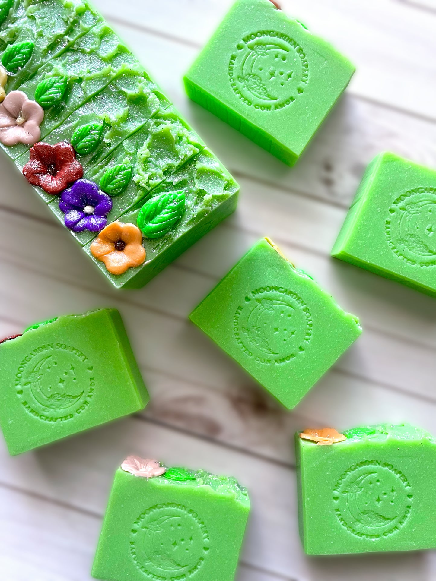 One small soap loaf topped with soap dough flowers surrounded by six handmade soap bars.