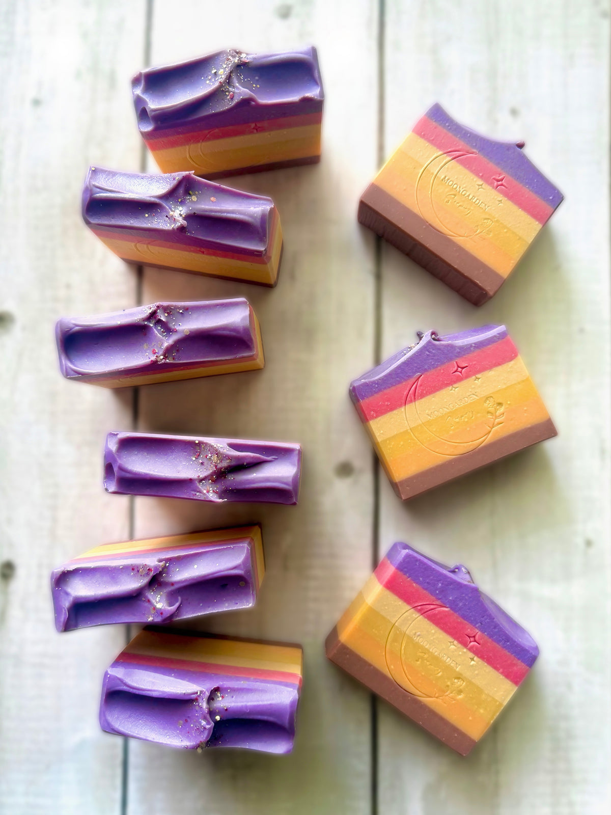 Ten handmade soap bars, arranged on a white rustic wooden background.