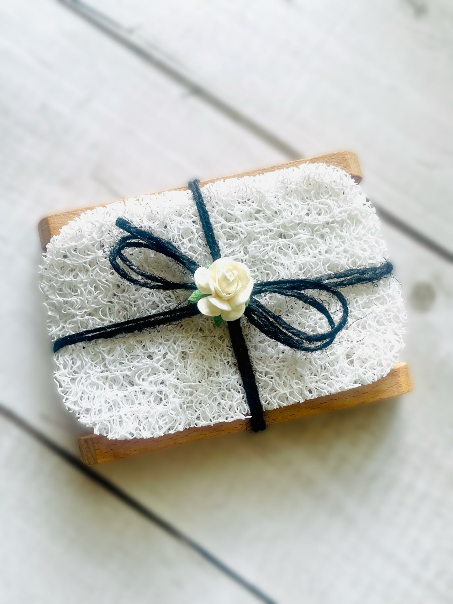 One soap dish with soap saver pad tied with black twine string and adorned with a paper rose on top. 