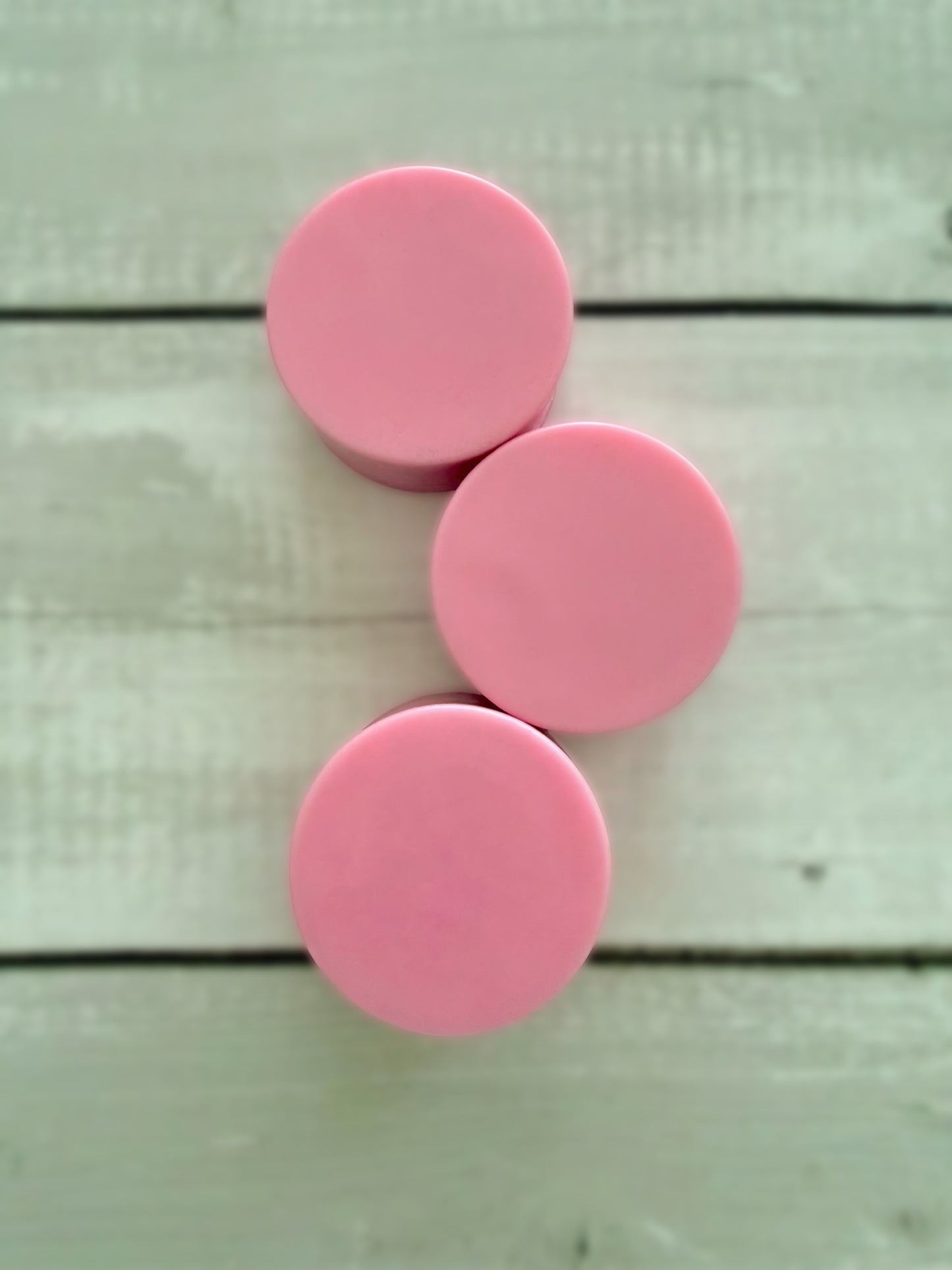 Three pink solid conditioner bars, arranged on a rustic wooden background.