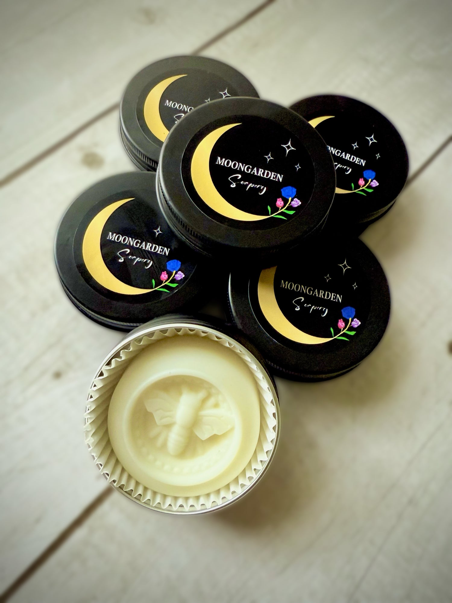 A stack of round tin jars with one open tin displaying a solid lotion bar. 