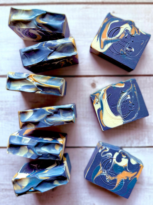 Nine bars of handmade soap bars in blue, yellow, and white, arranged on a white rustic wooden background. 
