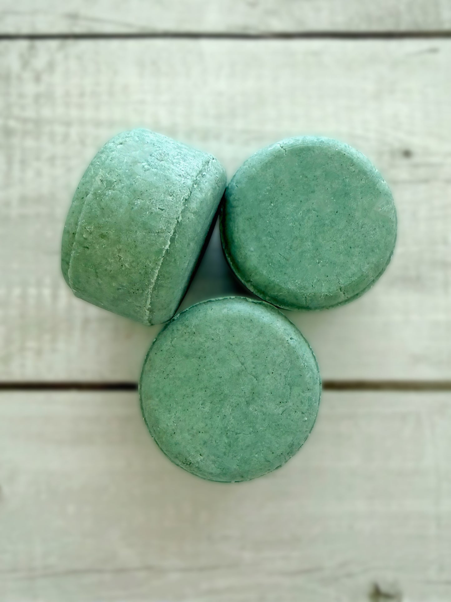 Three green solid shampoo bars, arranged on a rustic wooden background. 