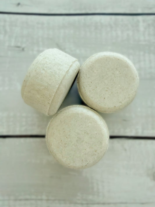 Three white solid shampoo bars, arranged on a rustic wooden background. 