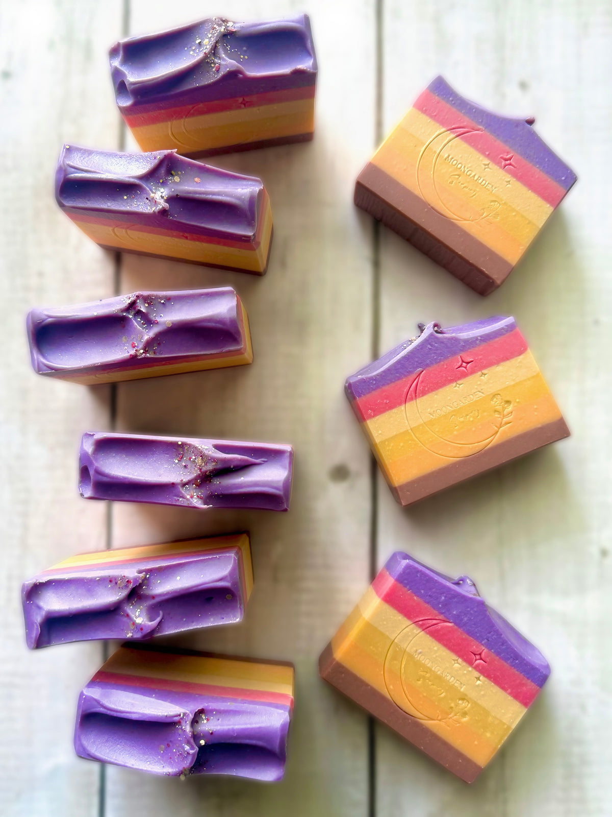 Ten handmade colorful striped soap bars, arranged on a white rustic wooden background. 