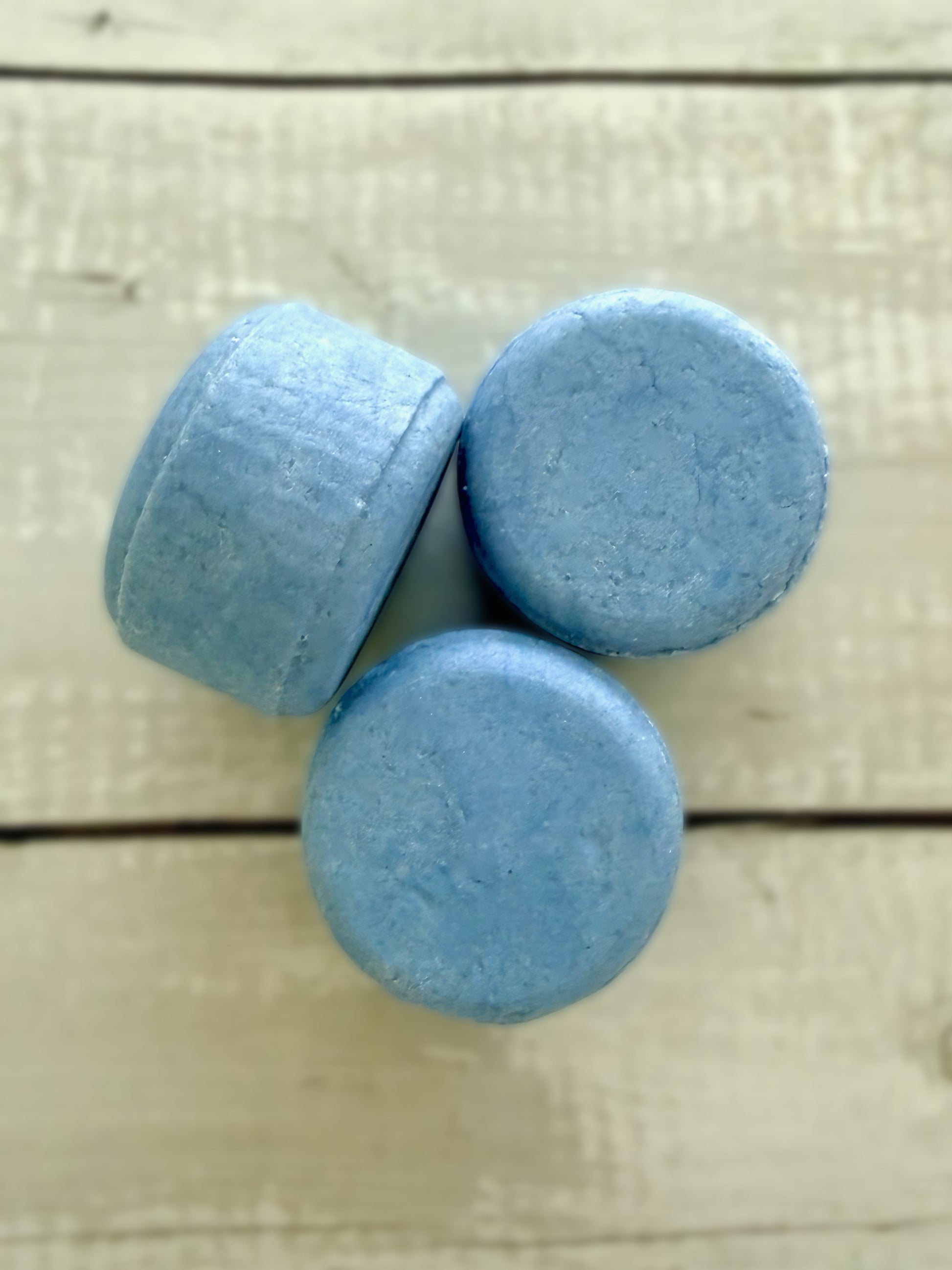 Three blue solid shampoo bars, arranged on a rustic wooden background. 