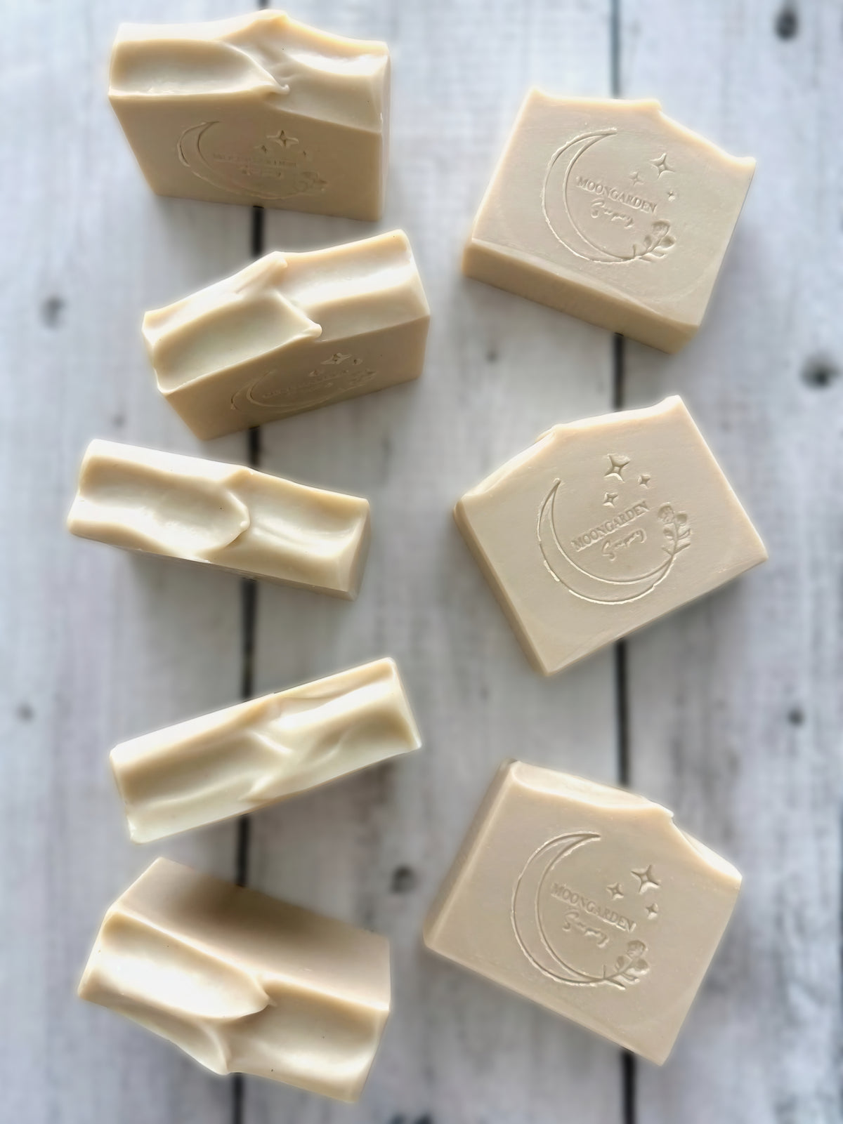 Nine white handmade soap bars, arranged on a white rustic wooden background. 