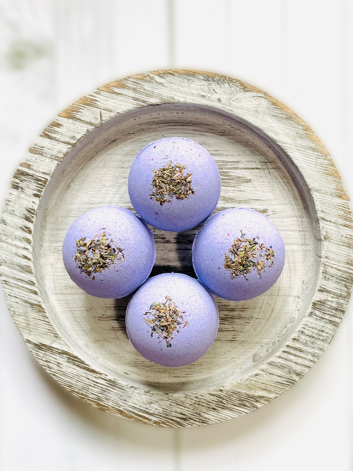 Four lavender bath bombs on a round wooden serving tray. 