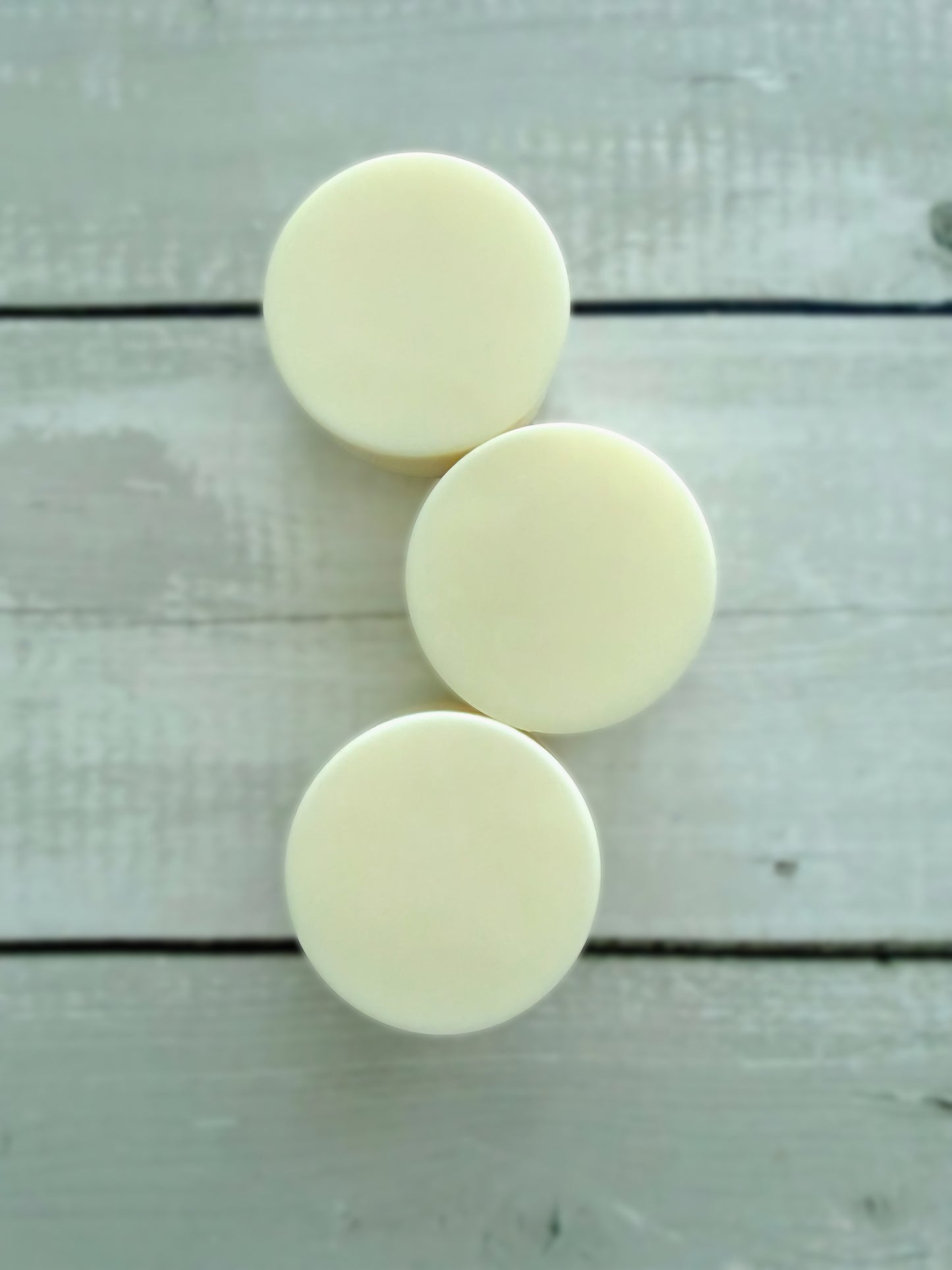 Three white solid conditioner bars, arranged on a rustic wooden background. 