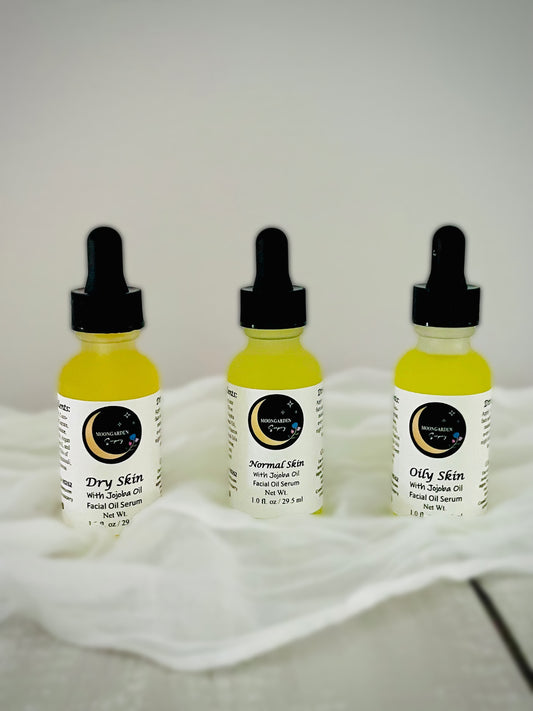 Three small dropper bottles of facial oil arranged on a white fabric surface against a light gray background. 