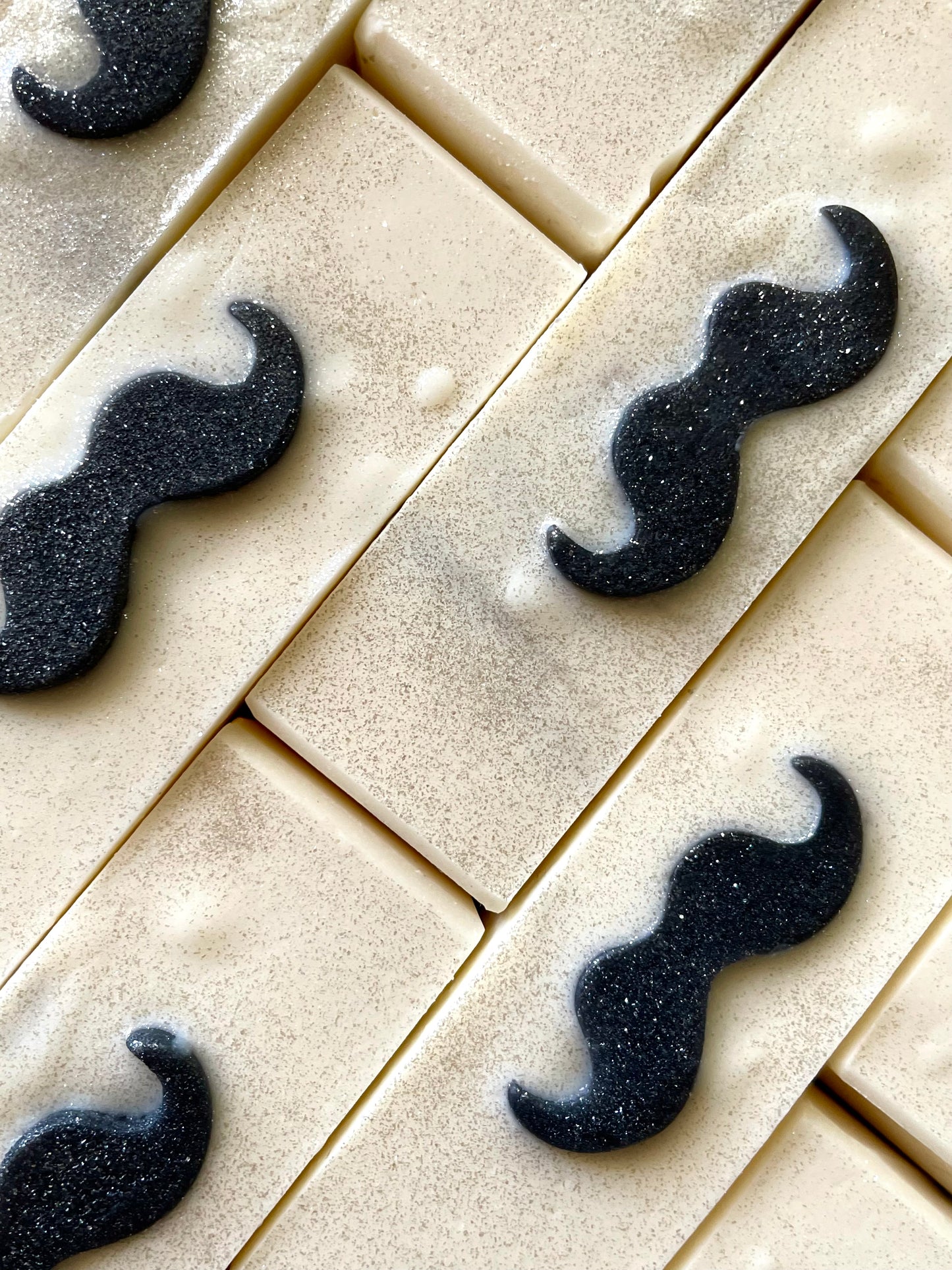 A closeup of the tops of The Local Barber barbershop bar soaps. Each bar soap has a mustache soap embed on top.