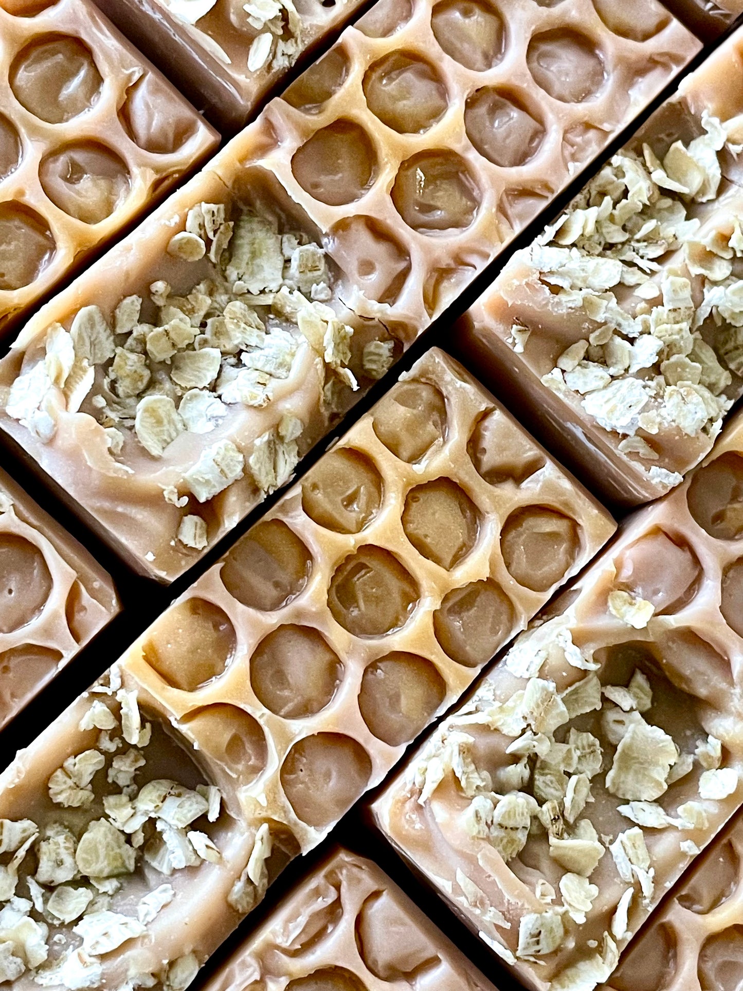 A closeup of the tops of Hall and Oats oatmeal, milk and honey bar soaps.  Each bar is topped with whole oats on the left side with a honeycomb imprint on the right side. 